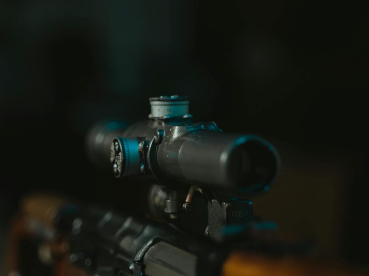 Detailed shot of a rifle scope on a firearm, in low light setting.